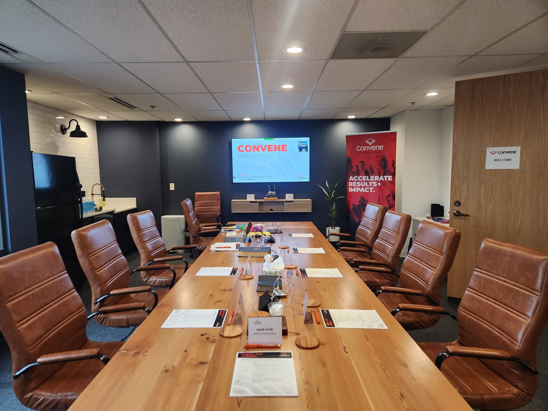 A Convene peer advisory team meeting room set for a purpose day — long conference table, materials at each seat, and the Convene logo on the screen.